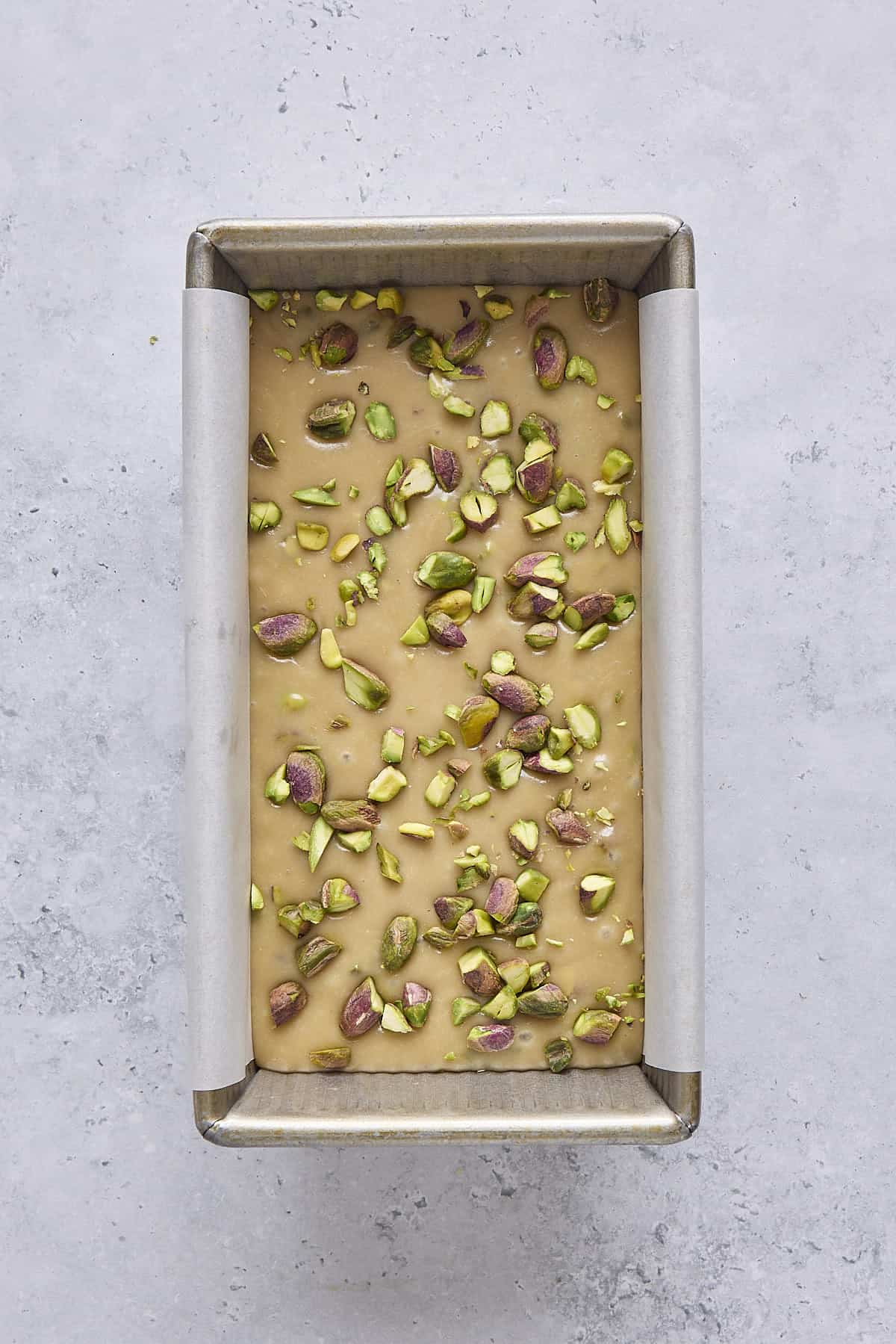 Recipe in a parchment lined loaf pan with extra pistachios on top before setting.