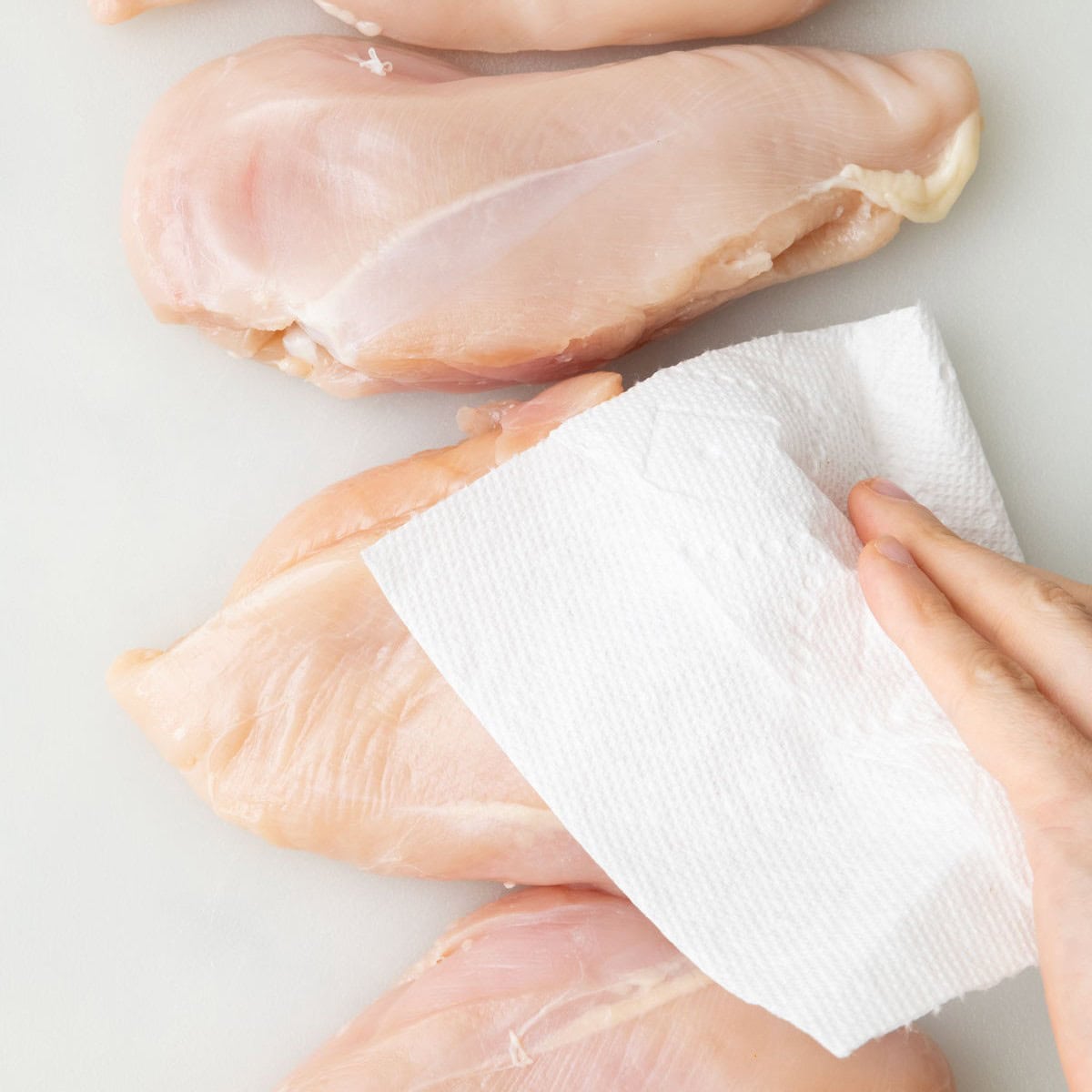 Chicken breasts on a cutting board being patted dry with paper towels.
