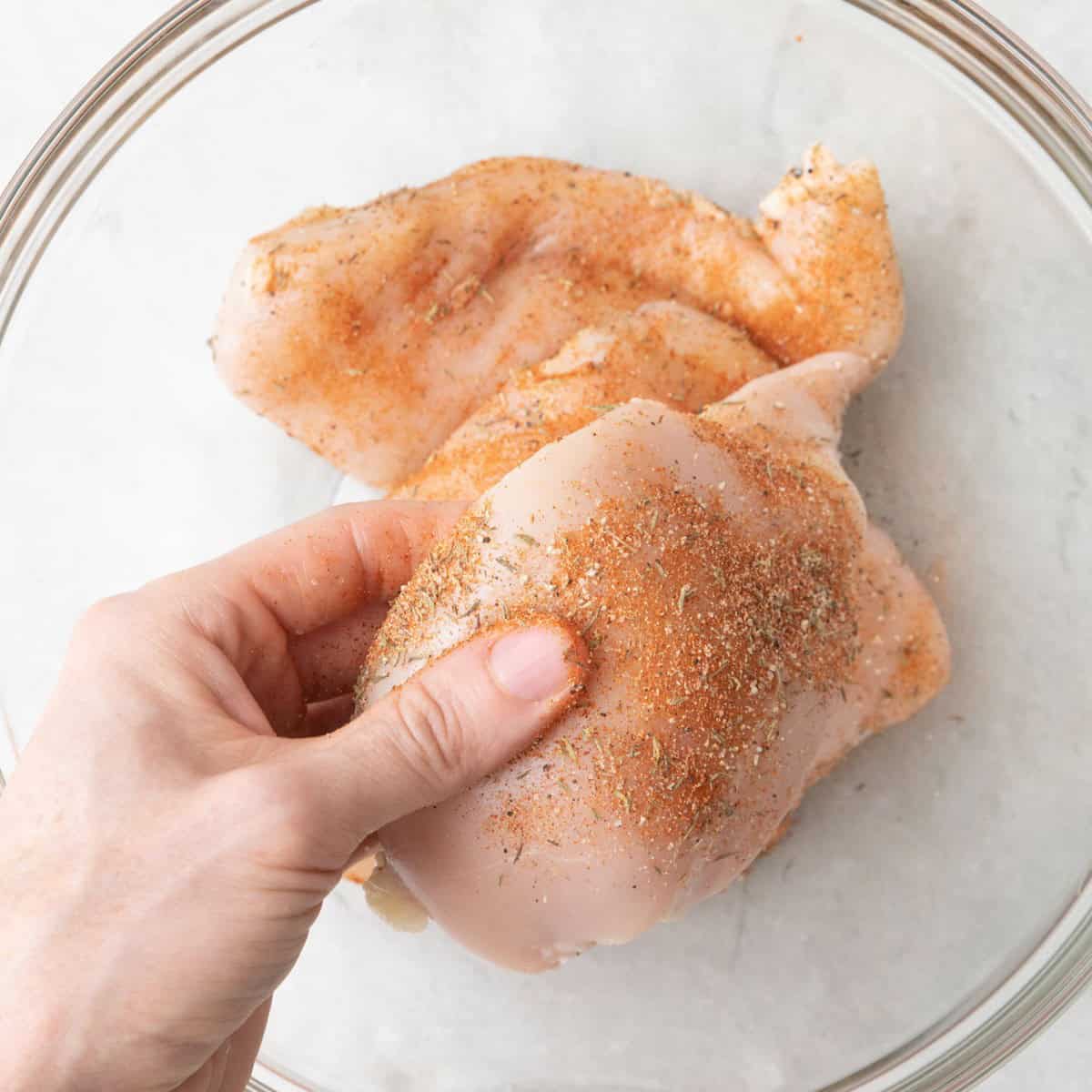 3 seasoned chicken breasts with a hand coating the last one with spices.
