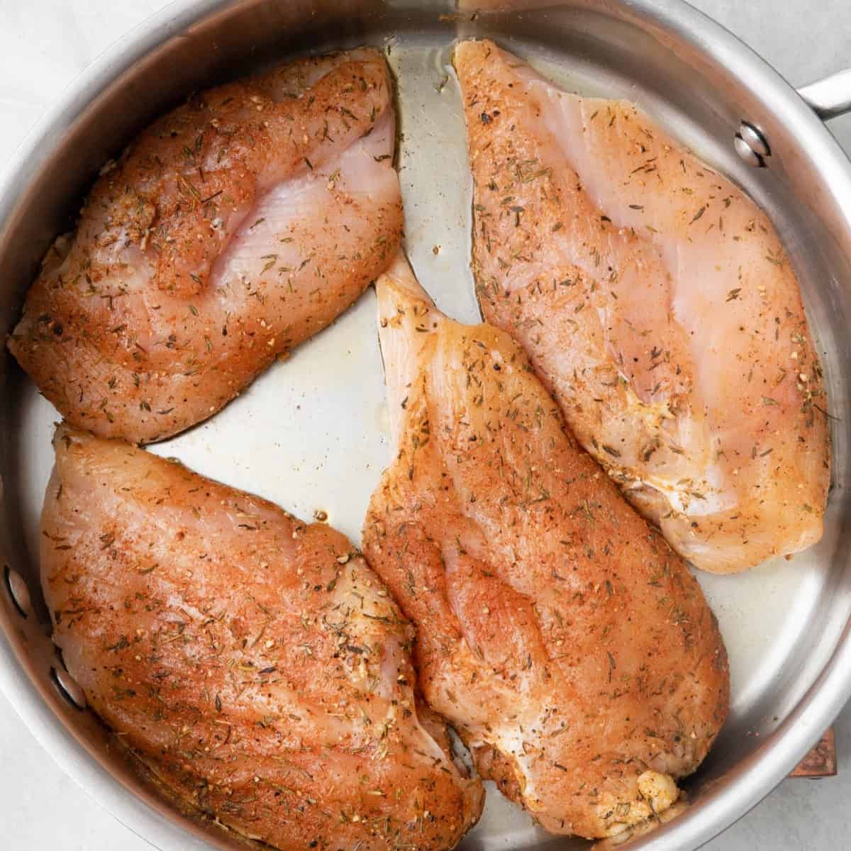 Seasoned chicken breast in an oiled pan.