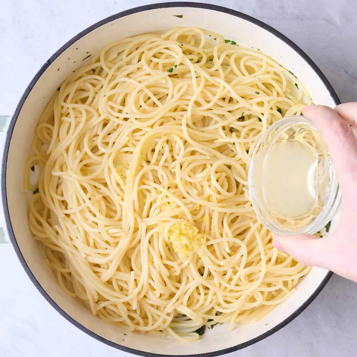After cooking with lemon zest, pasta water, and pasta added, and juice being poured in from a small dish