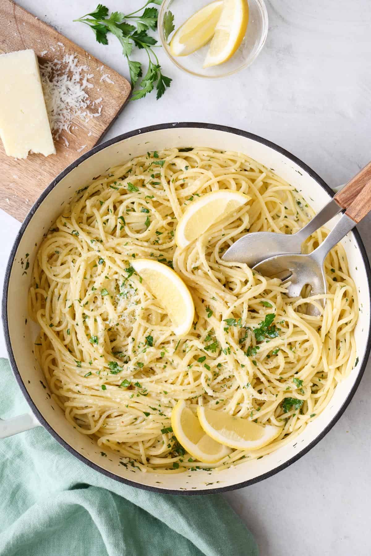 Lemon Pasta in pan with lemon wedges, extra grated parm and chopped parsley sprinkled on top, serving set dipped inside.