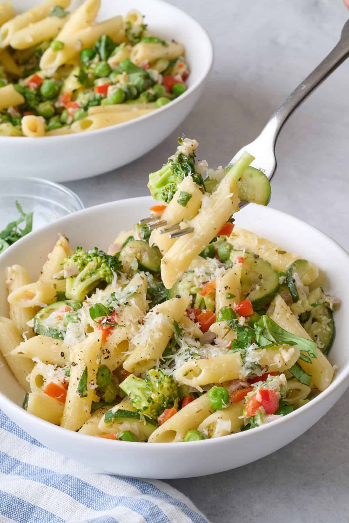 Fork lifting up a bite of homemade pasta primavera from a bowl.