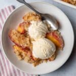 Peach crisp in a bowl served with two scoops of vanilla ice cream