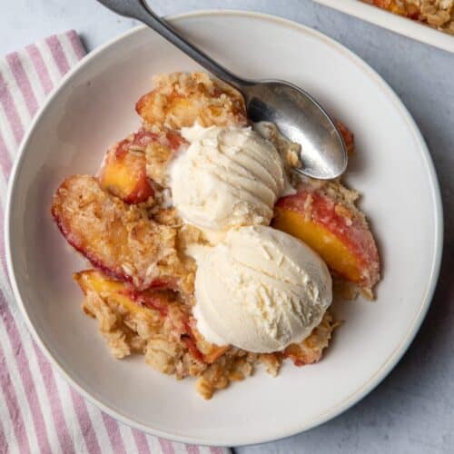 Peach crisp in a bowl served with two scoops of vanilla ice cream