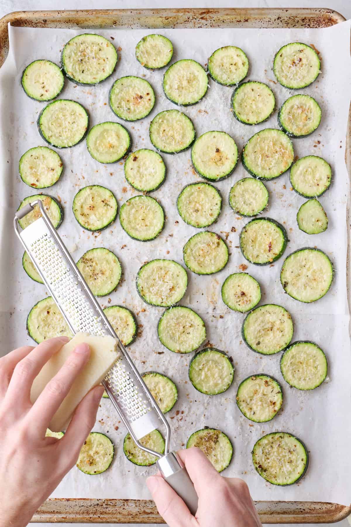 Grating parmesan over zucchini rounds after roasting.