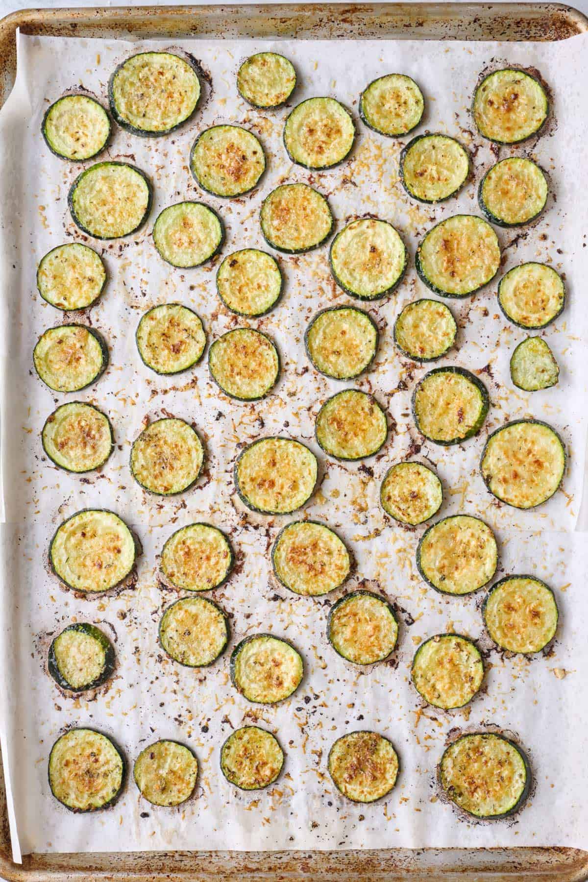 Baked zucchini rounds with parmesan cheese on sheet pan.