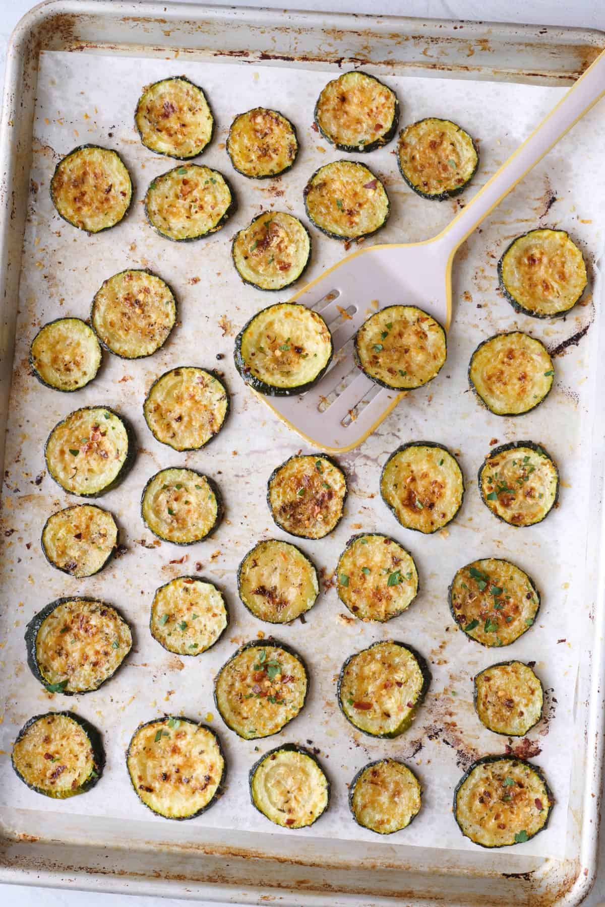 Oven roasted zucchini with toasted parmesan on a sheet pan with spatula.