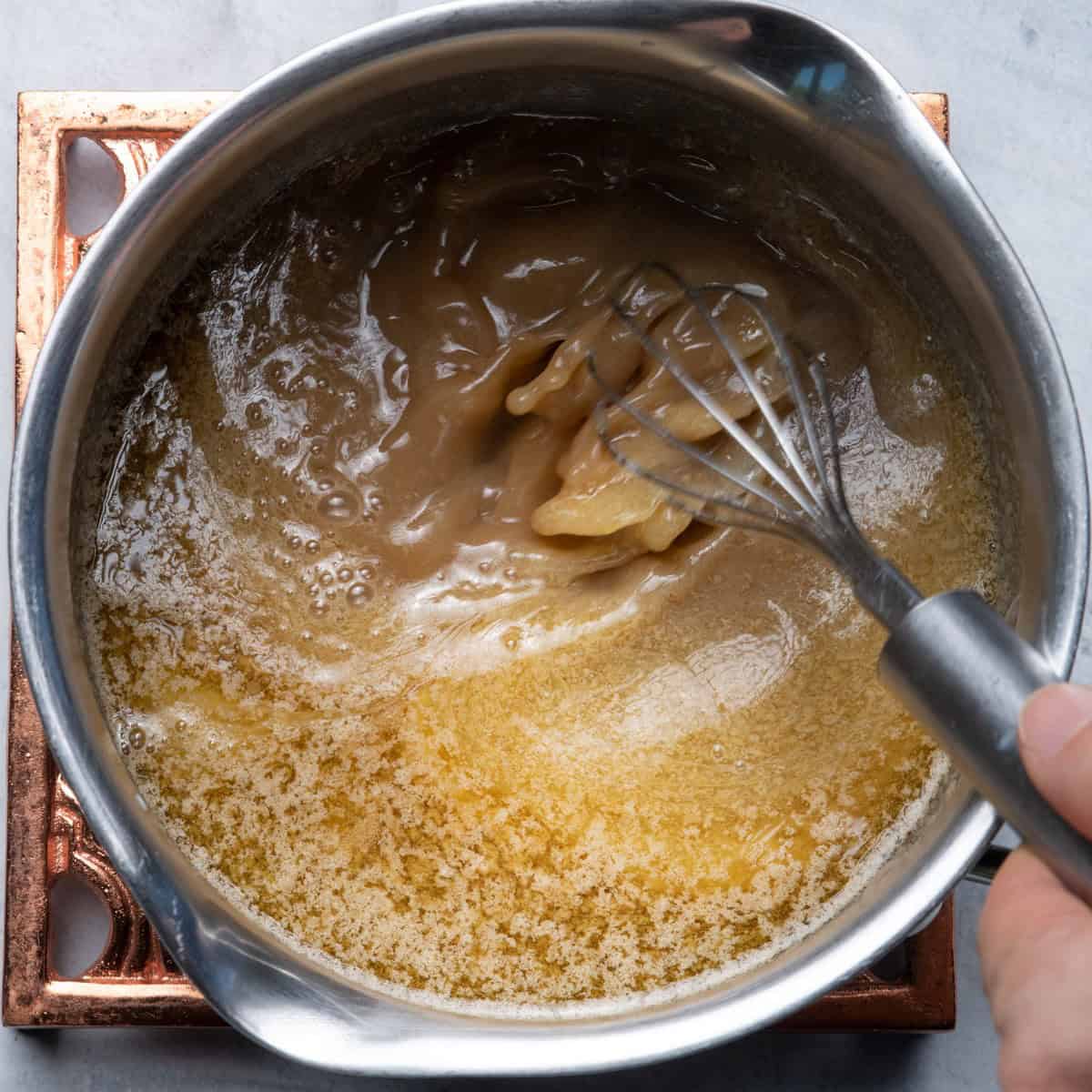 Whisking sugars and butter in pot.