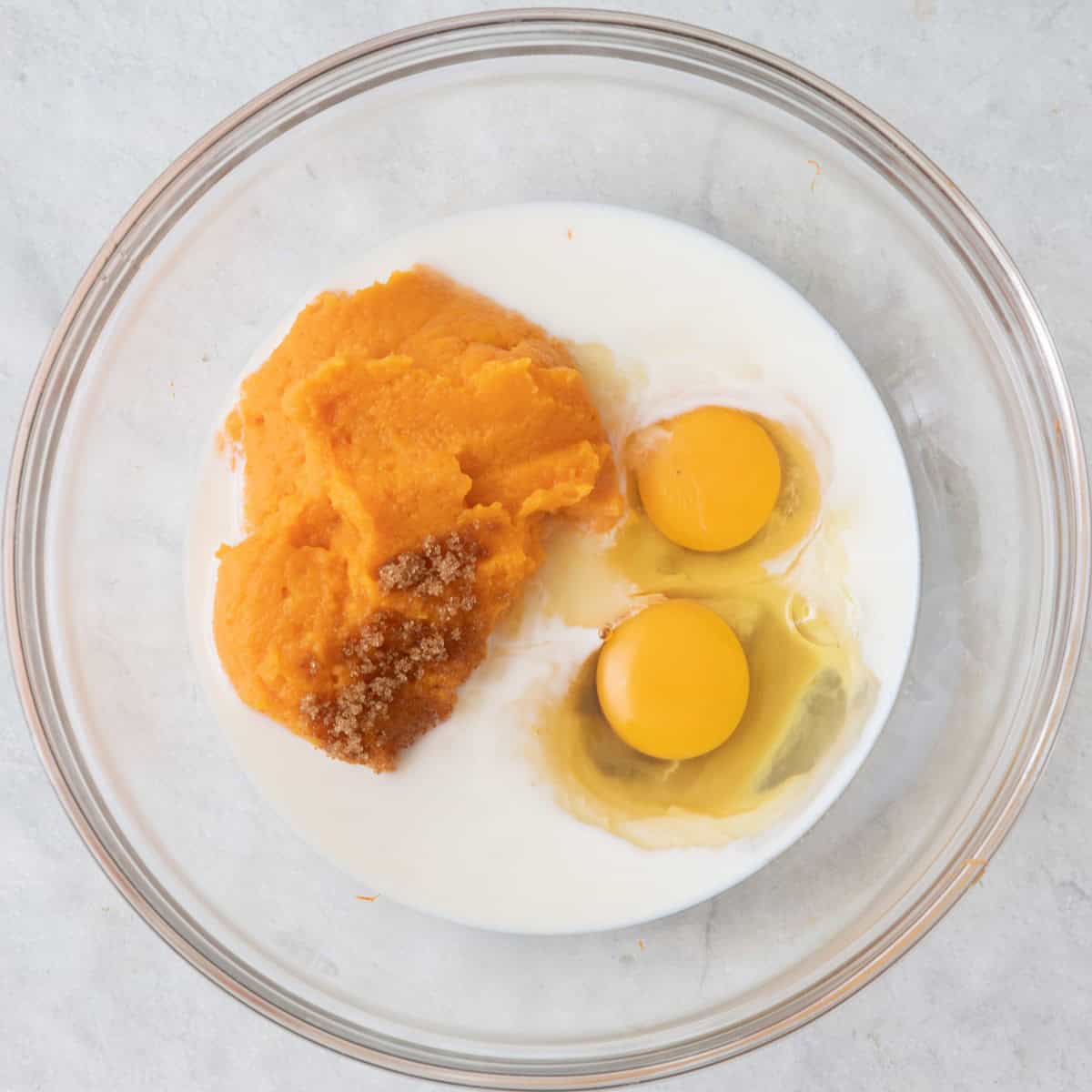 Eggs, milk, sugar, and cooked sweet potato in a bowl.