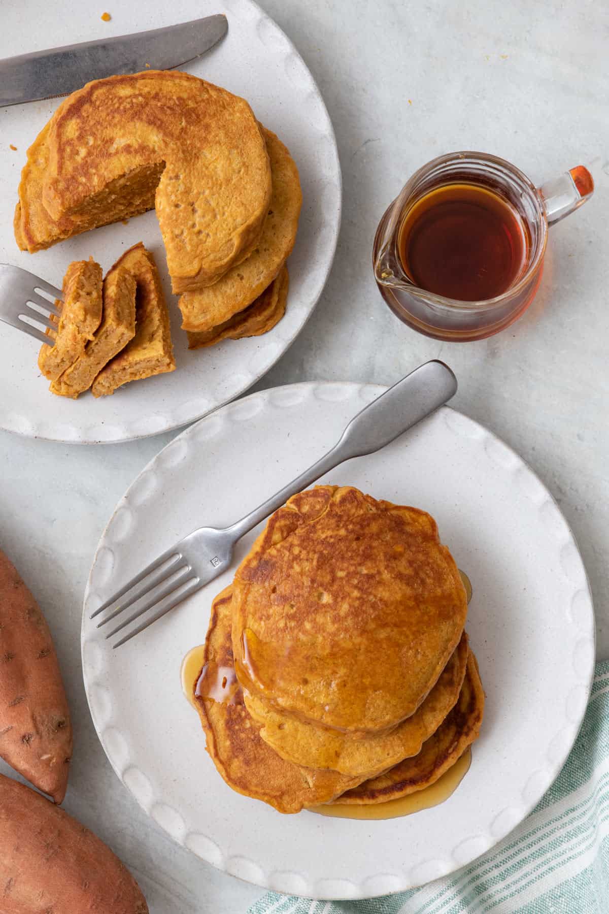 Two plates of sweet potato pancakes with syrup nearby.