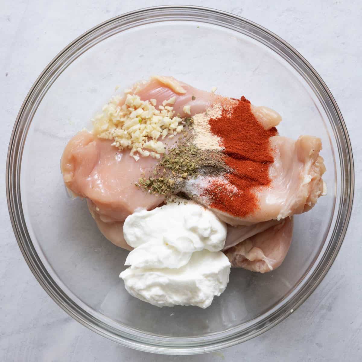 Yogurt and seasonings on top of chicken in a bowl.