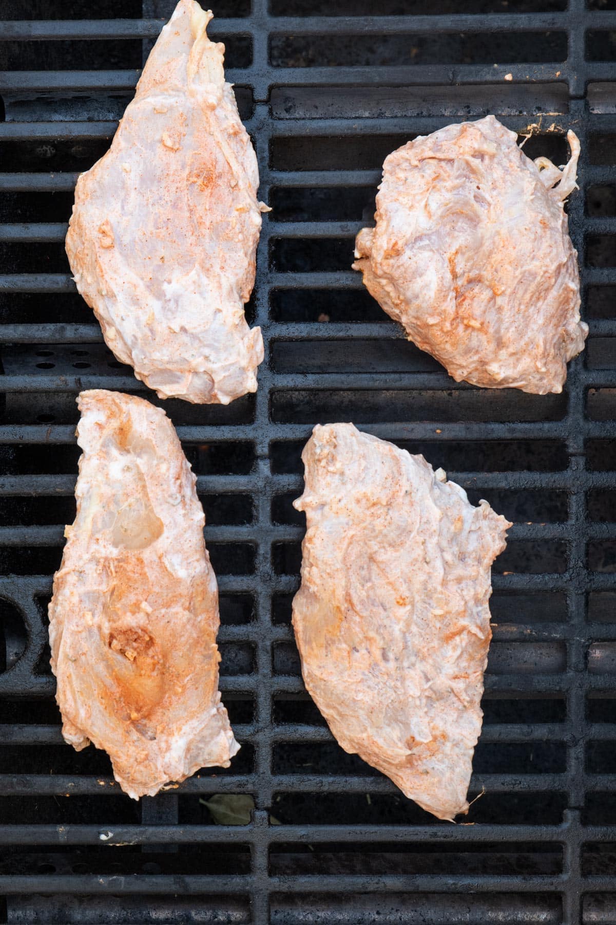 Yogurt marinated chicken breasts on an outdoor grill before cooked.