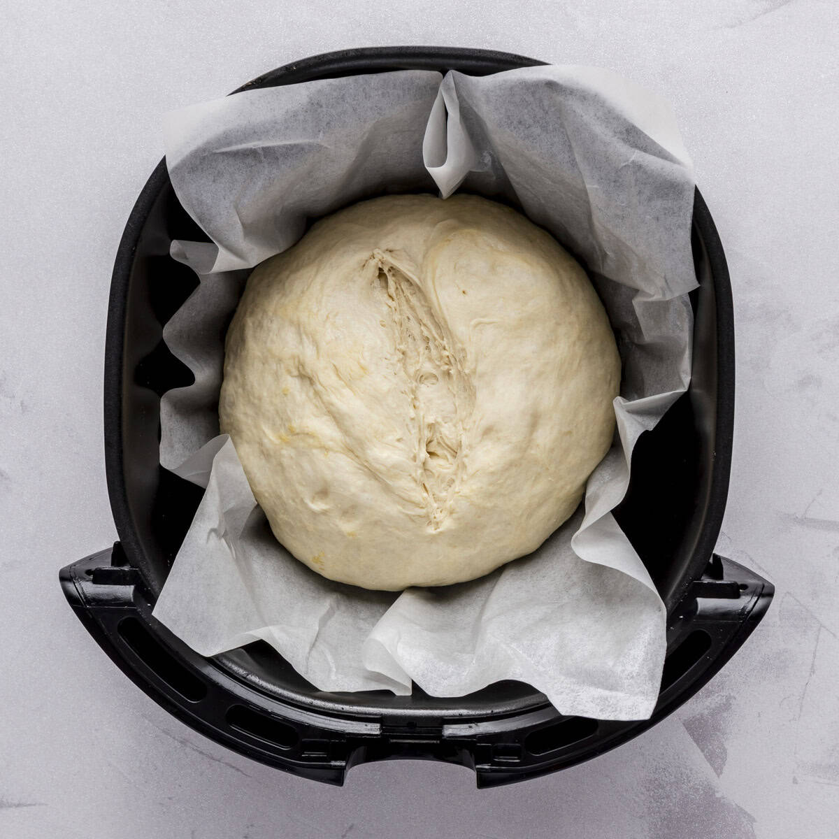Dough after its second rise with a ยฝ inch deep cut on top and placed in the air fryer basket with parchment paper.