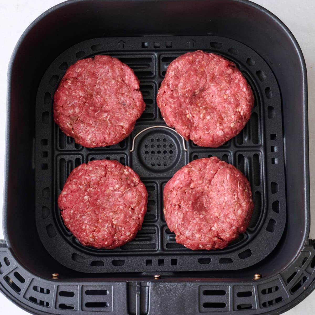 Hamburger patties in an air fryer basket before cooking.