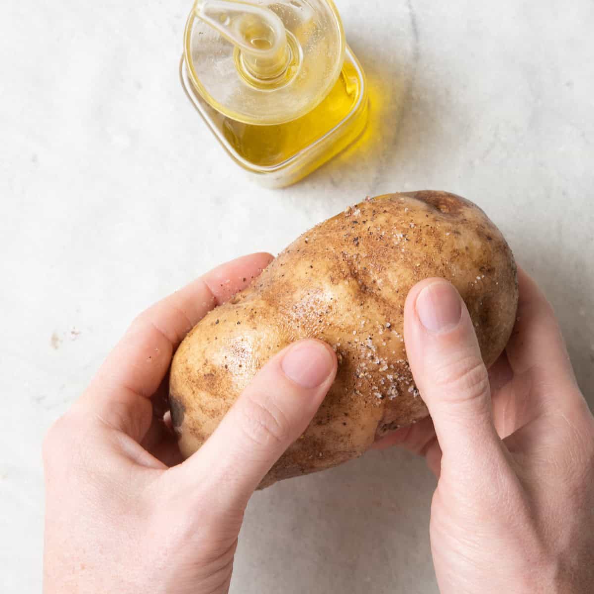 Hands rubbing oil and seasoning over potatoes.