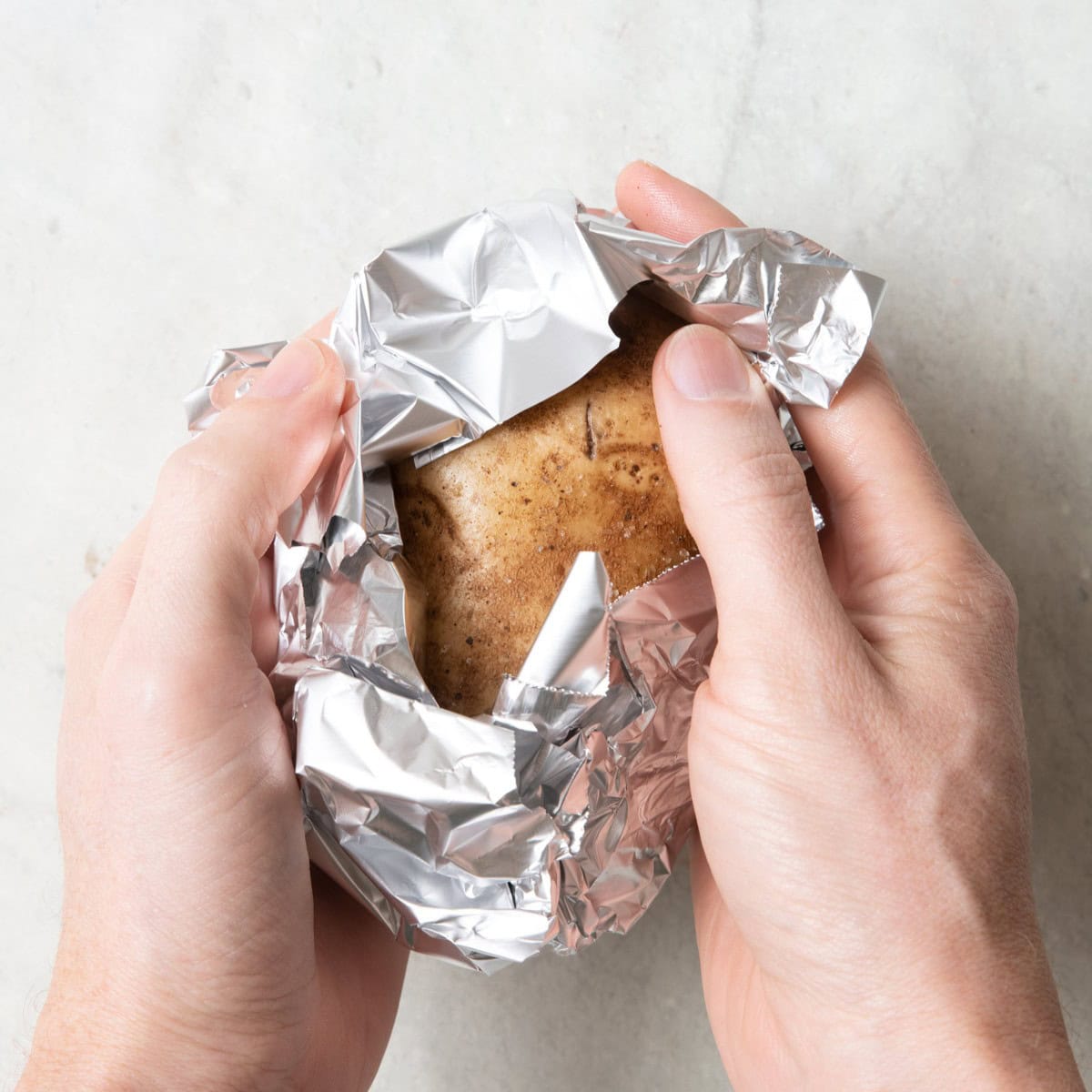 Wrapping potato with foil with hand closing the foil partially around one.