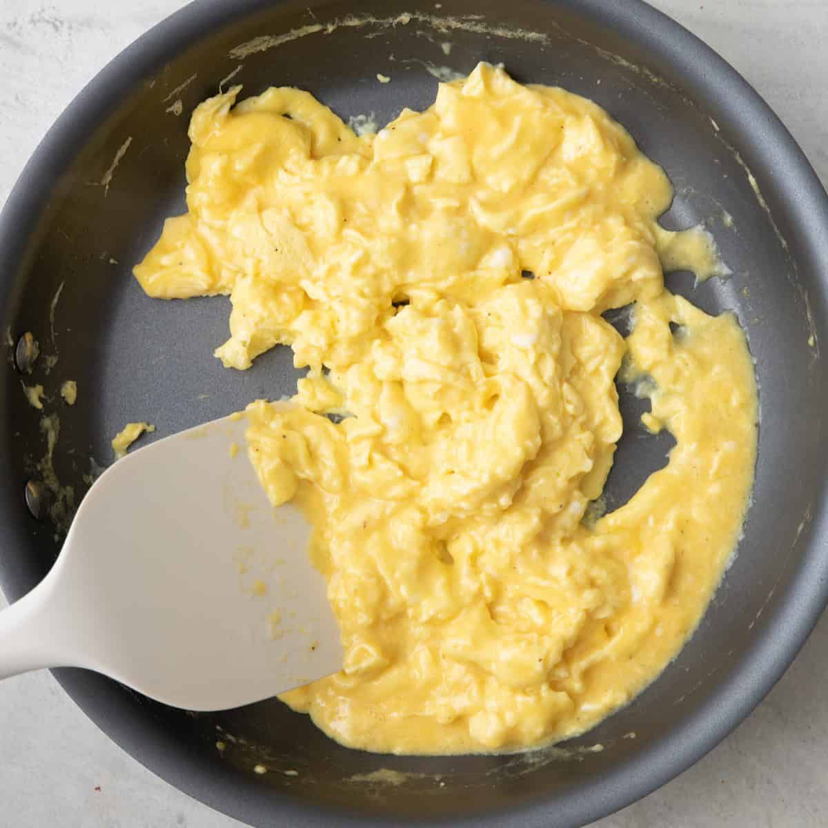Stirring partially cooked eggs with some liquid still showing.