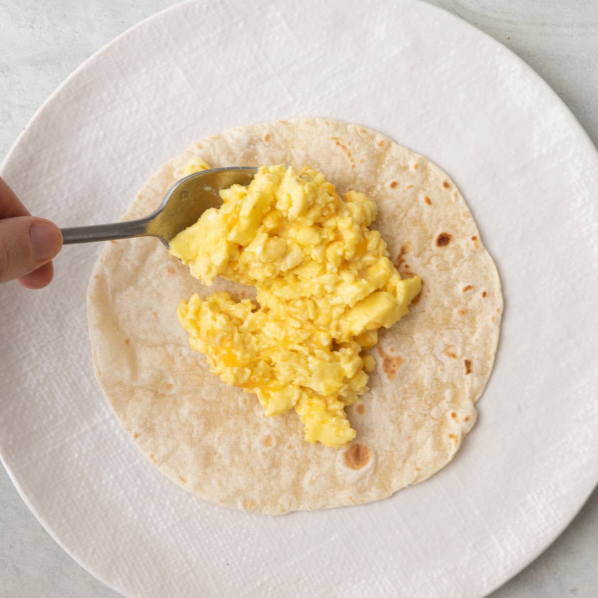 Adding cheesy eggs to a tortilla.