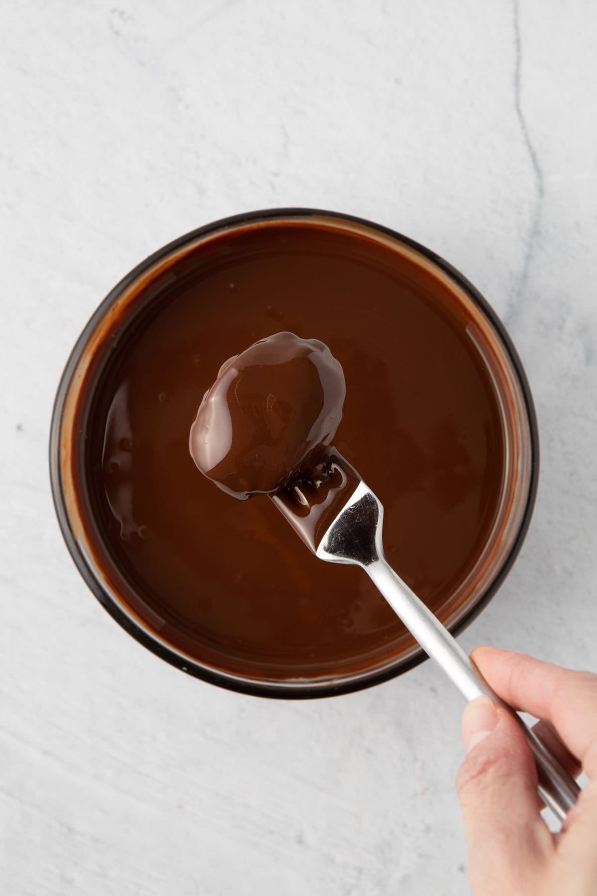 Peanut butter egg being removed from the melted chocolate with a fork lifted above the bowl.