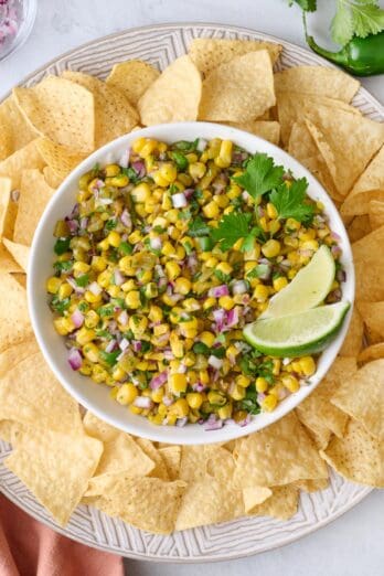Corn salsa in a bowl on a platter with tortilla chips.