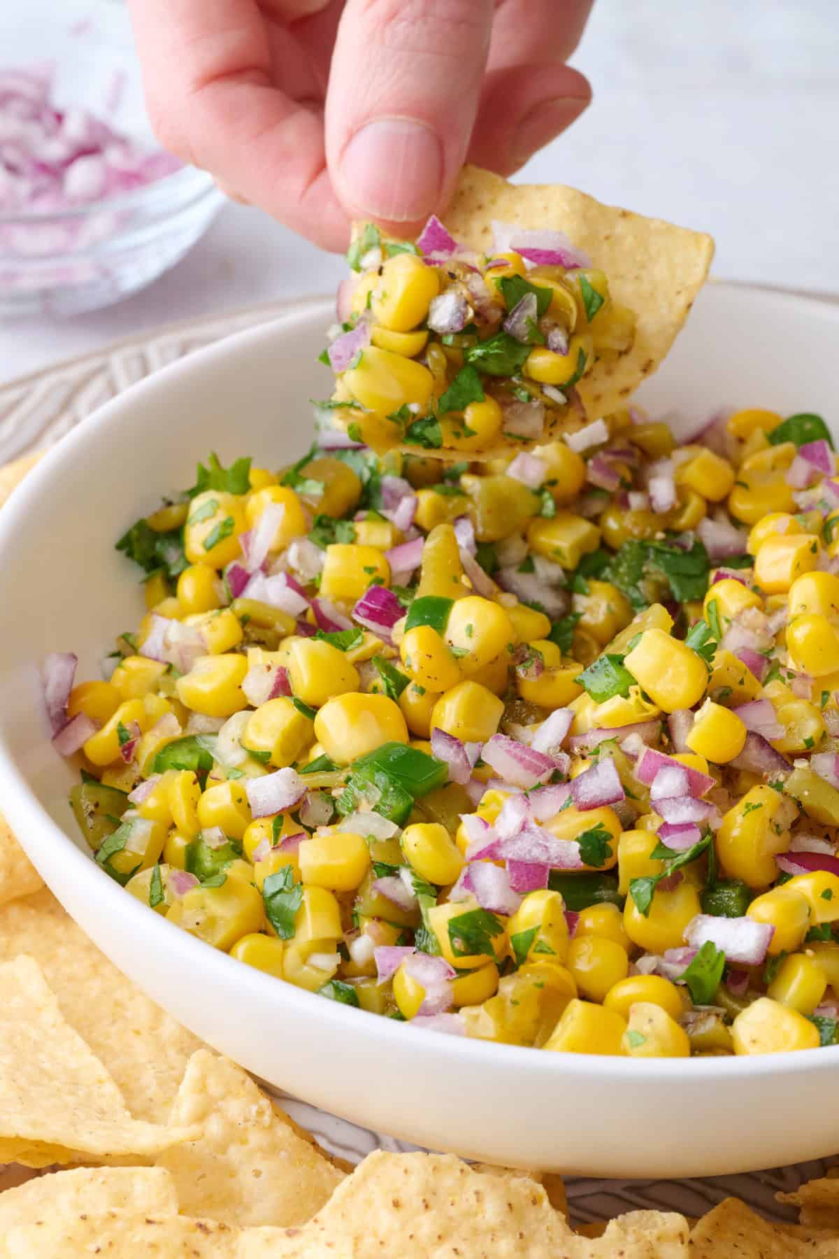 Hand lifting up corn salsa on a tortilla chip over bowl.
