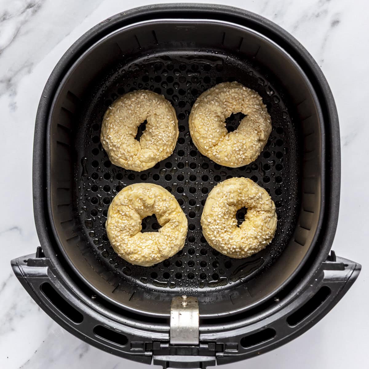 4 bagels in an air fryer basket with egg wash and sesame seeds baking cooking.