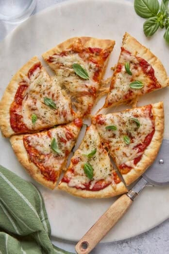 Cottage cheese pizza garnished with basil leaves, cut into 6 large slices with one slice pulled away, pizza cutter nearby.