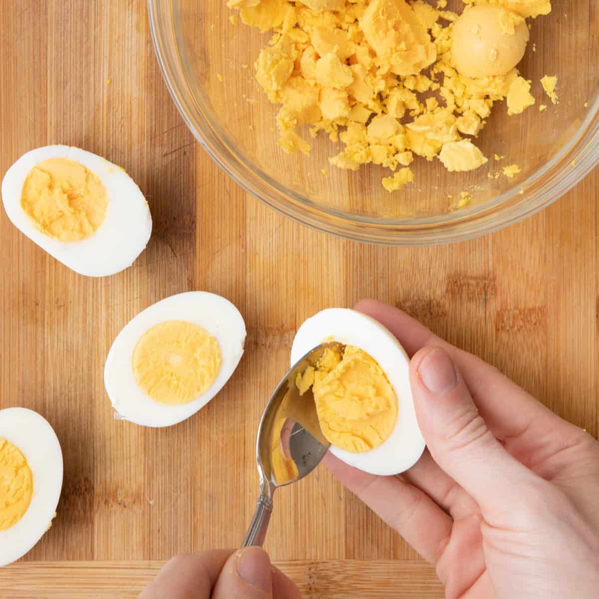 Spoon scooping out yolk over a bowl with some yolks already inside.