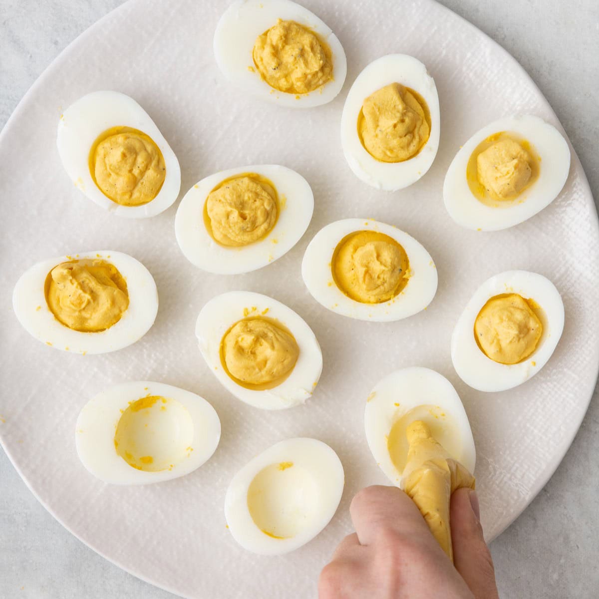 Piping yolk mixture into egg white shells at the end to show it filled completely.