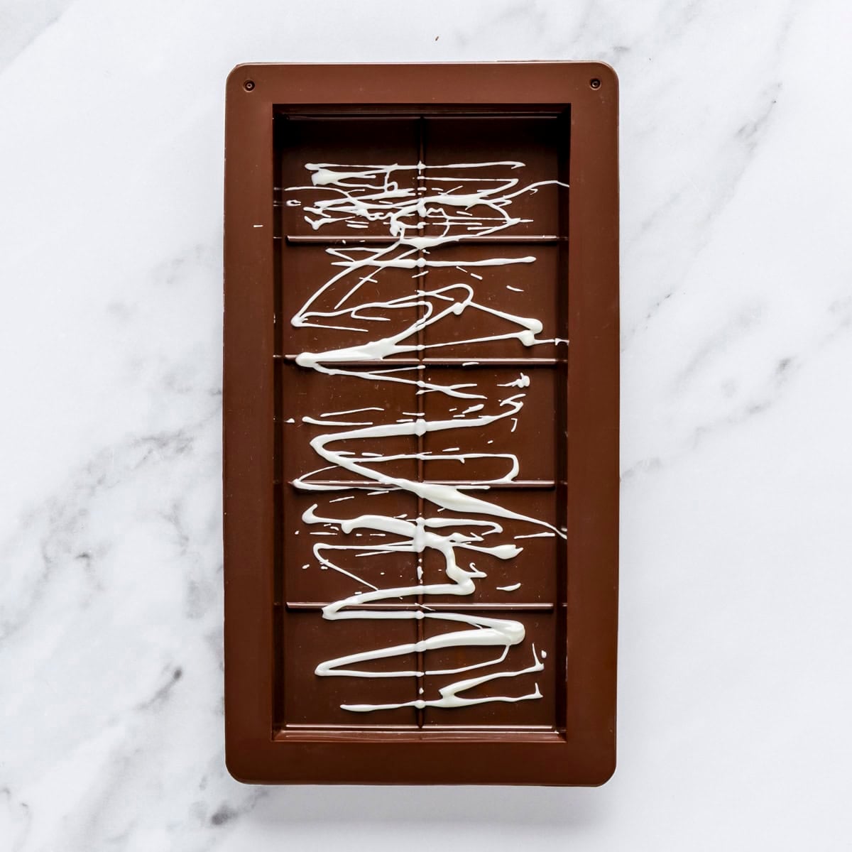 White chocolate drizzled over chocolate bar mold.