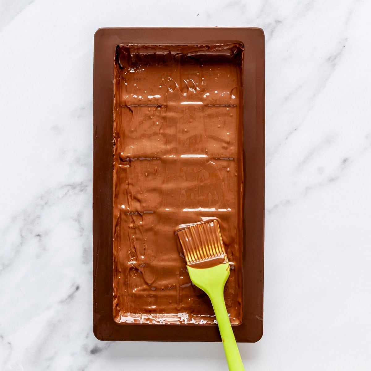 Pastry brush spreading melted milk chocolate over mold.