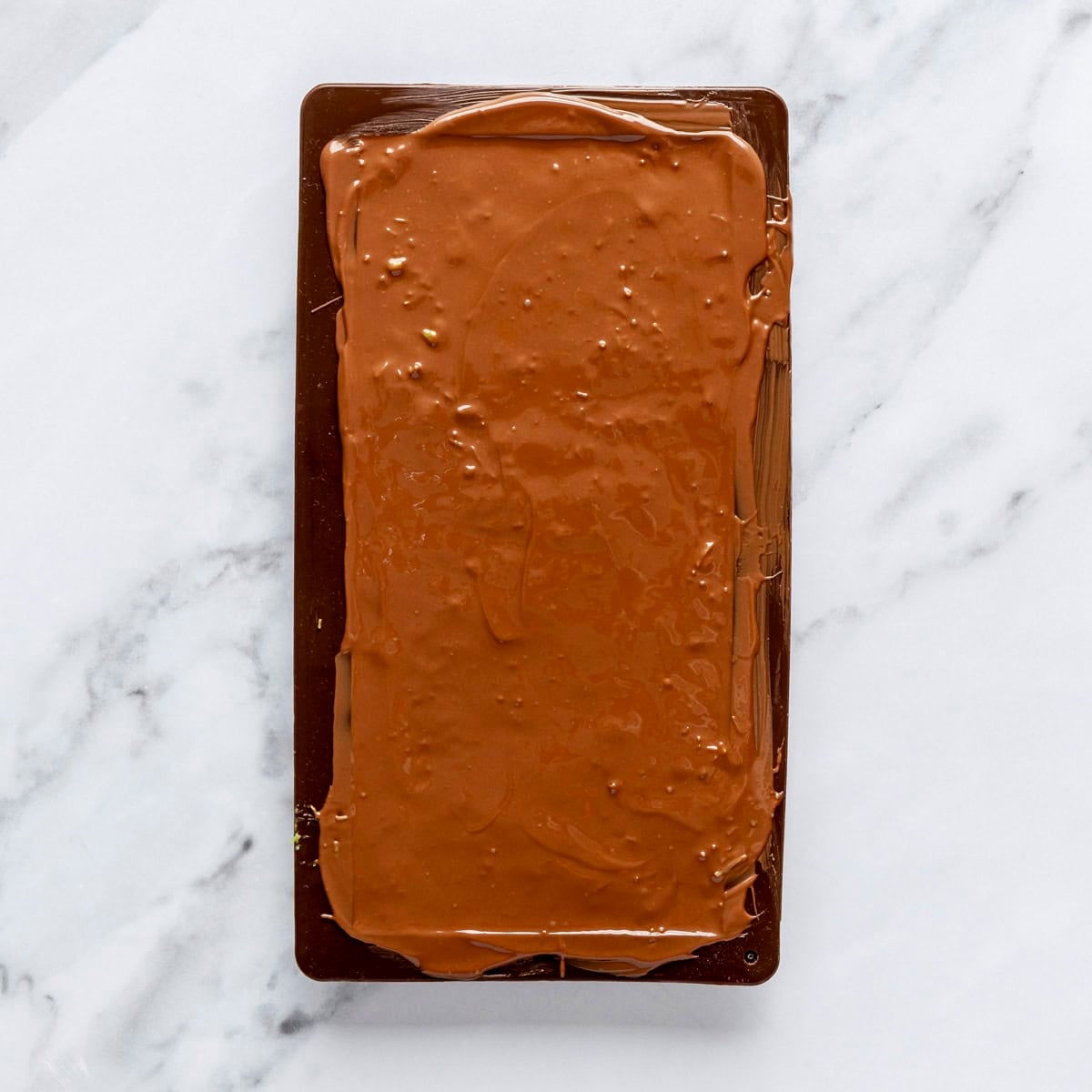 Melted chocolate layer over bar filling in mold.