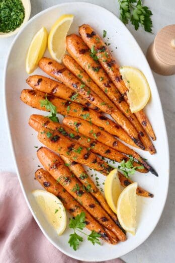 Grilled carrots on a platter, garnished with parsley and lemon wedges.