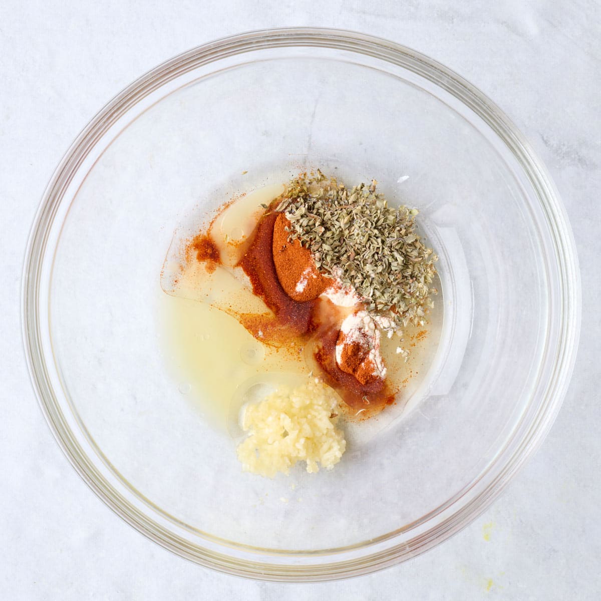 Oil, lemon, minced garlic, and spices in a bowl.