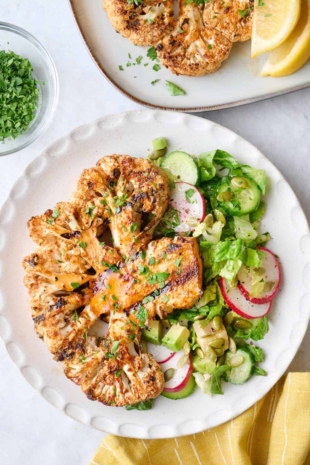 Grilled cauliflower steak on a plate with a light green salad.