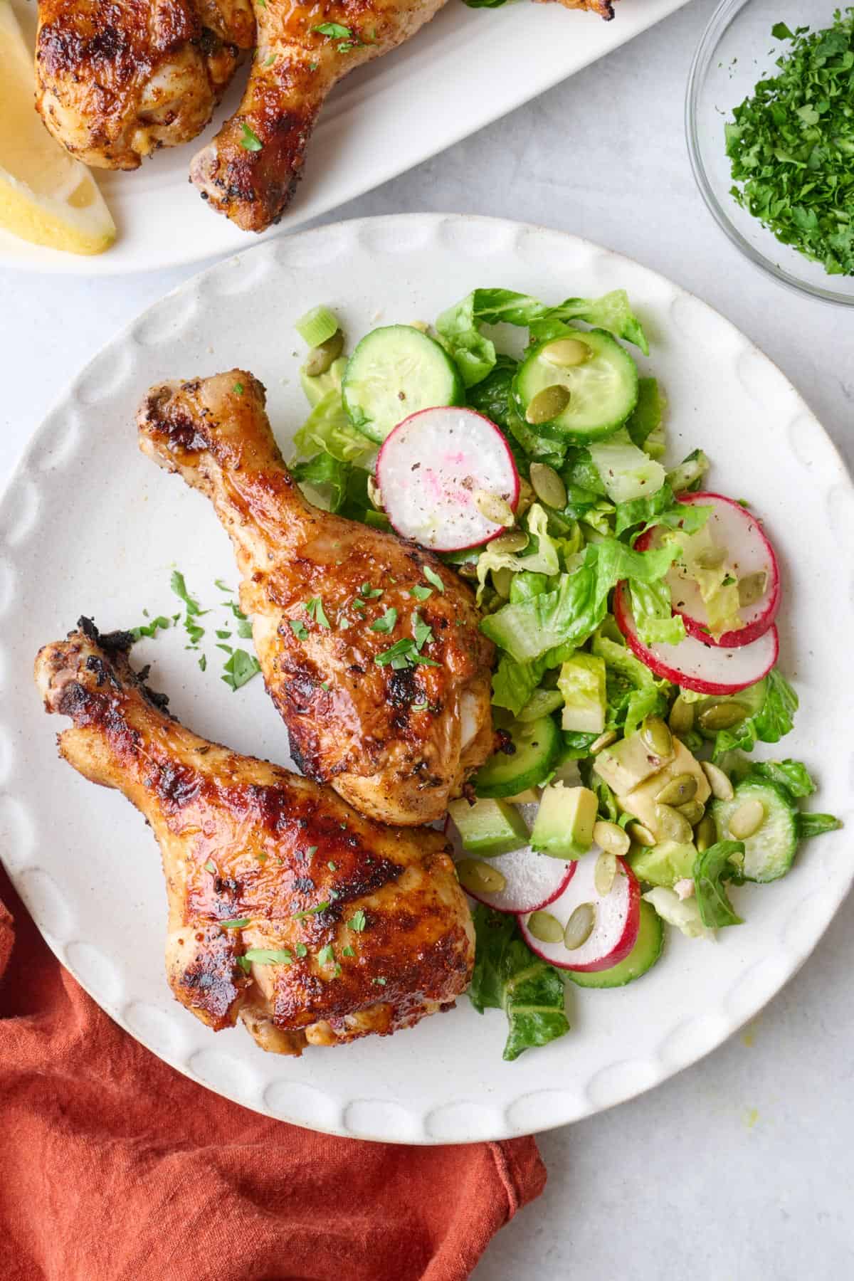 Two grilled chicken legs on a plate with a green salad.