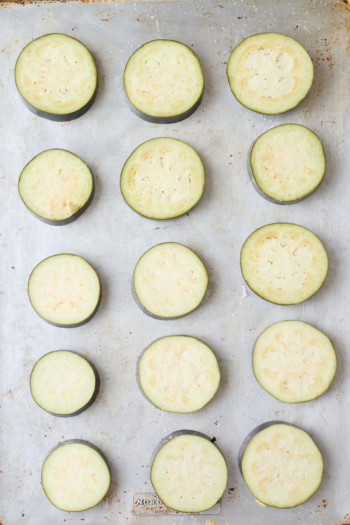 Eggplant rounds on a baking sheet with salt sprinkled on top.