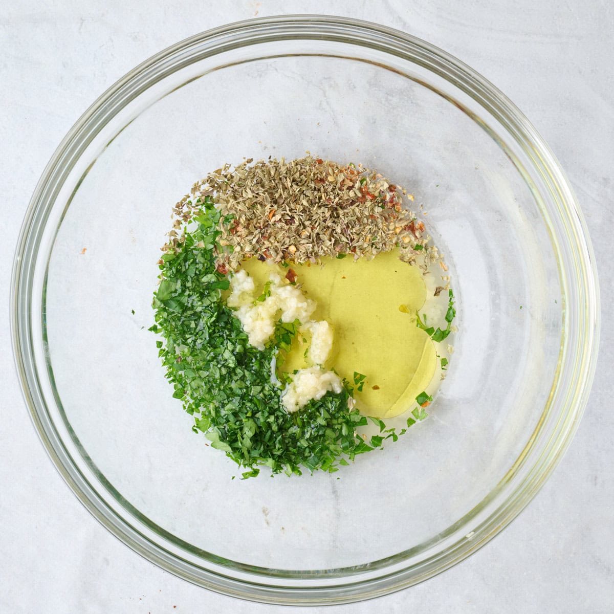 Olive oil, parsley, juice, garlic, oregano, and crushed red pepper in a bowl.