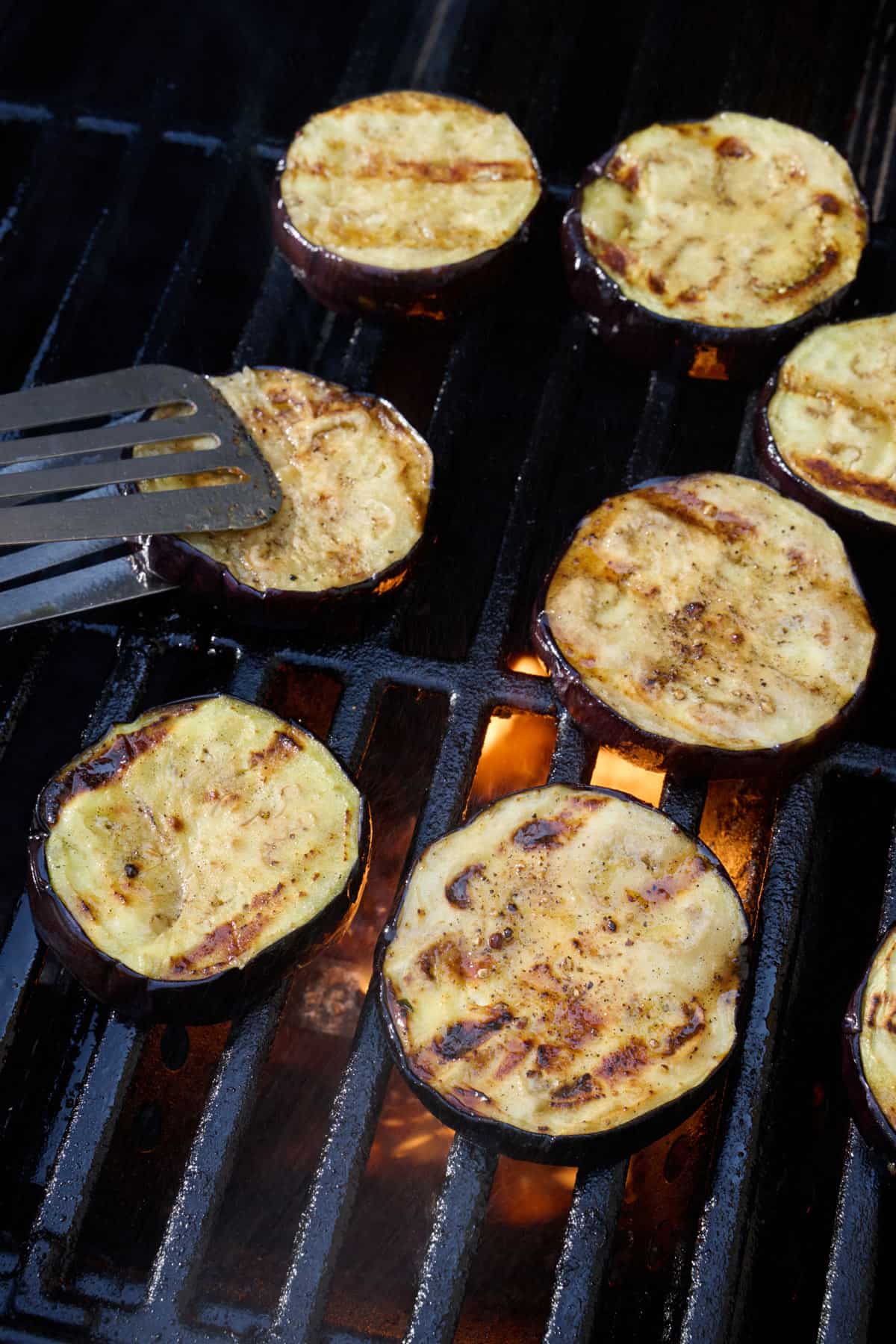 Eggplant slices on grill with tongs.