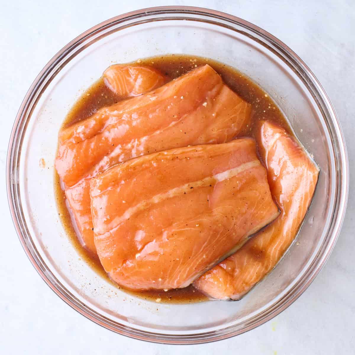 Salmon fillets added to bowl with marinade.