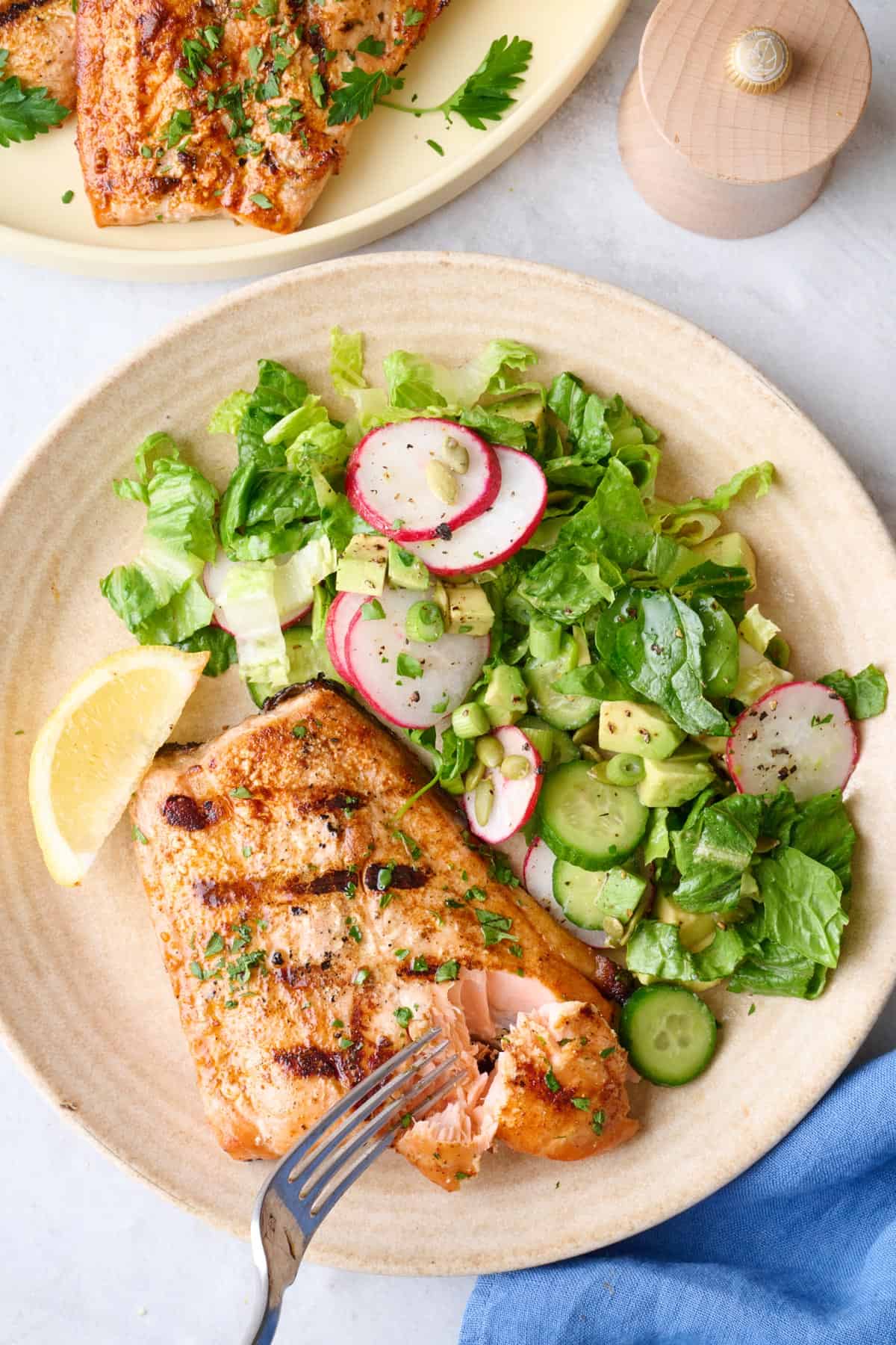 One grilled salmon on a plate with green salad, fork flaking end piece, platter nearby.