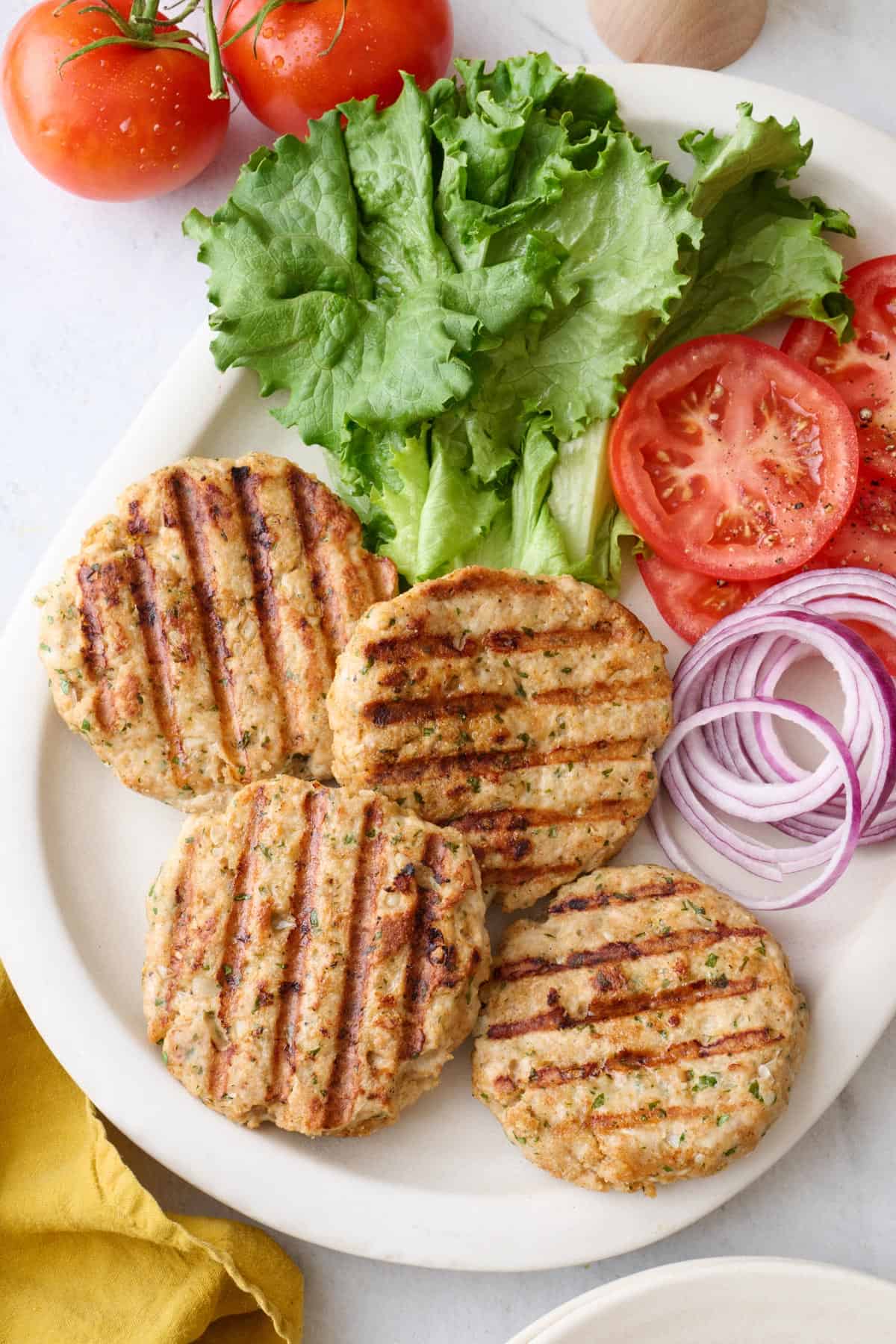 Ground chicken burger patties on a platter with lettuce, sliced tomatoes, and sliced red onions.
