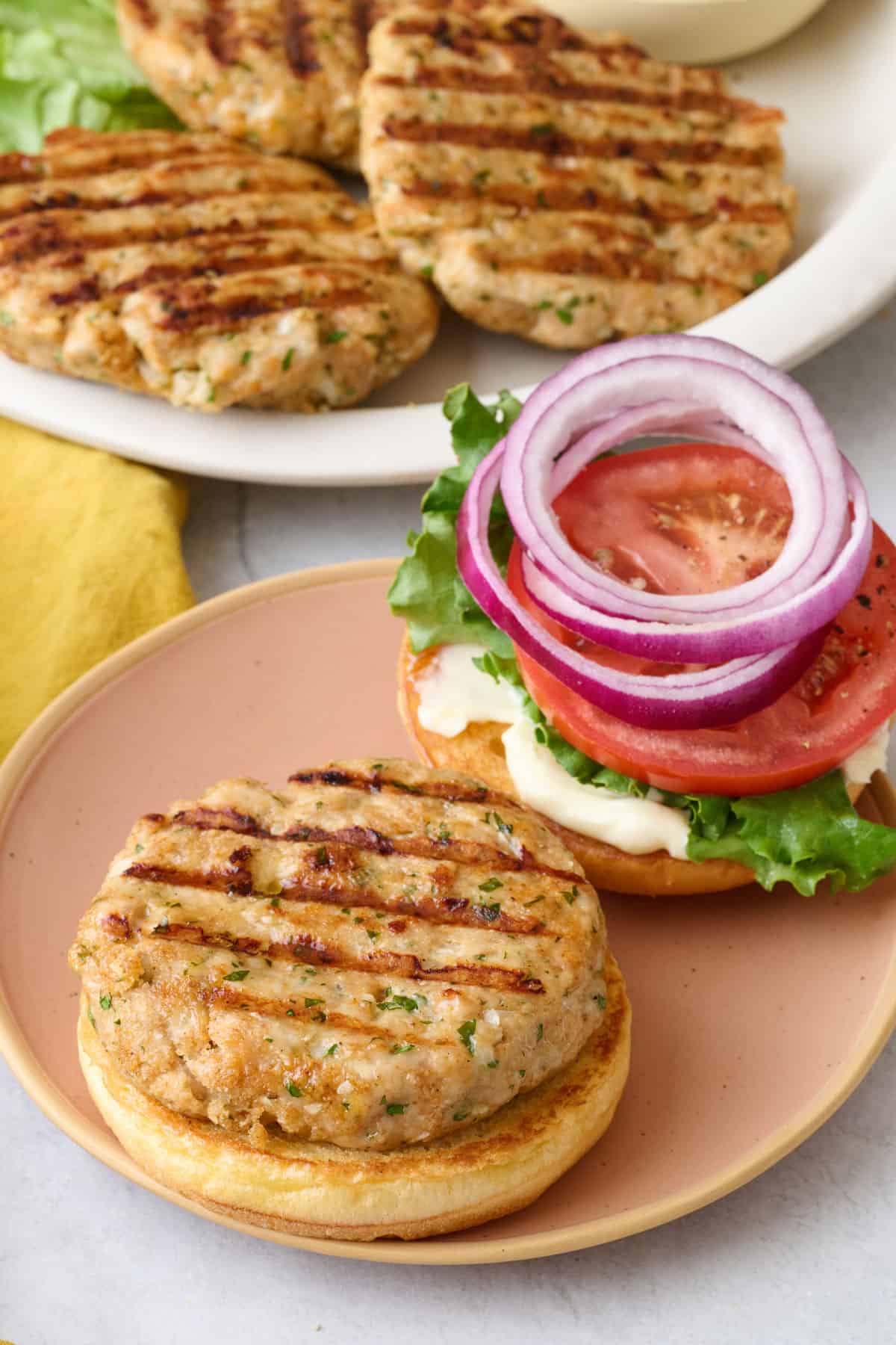 Open faced ground chicken burger with toppings on lid, small dish of mayo and platter nearby.
