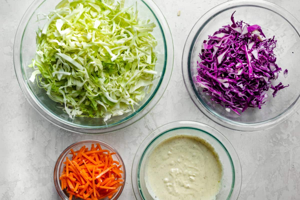 Ingredients for recipe: shredded green and red cabbages, shredded carrots, and slaw dressing.
