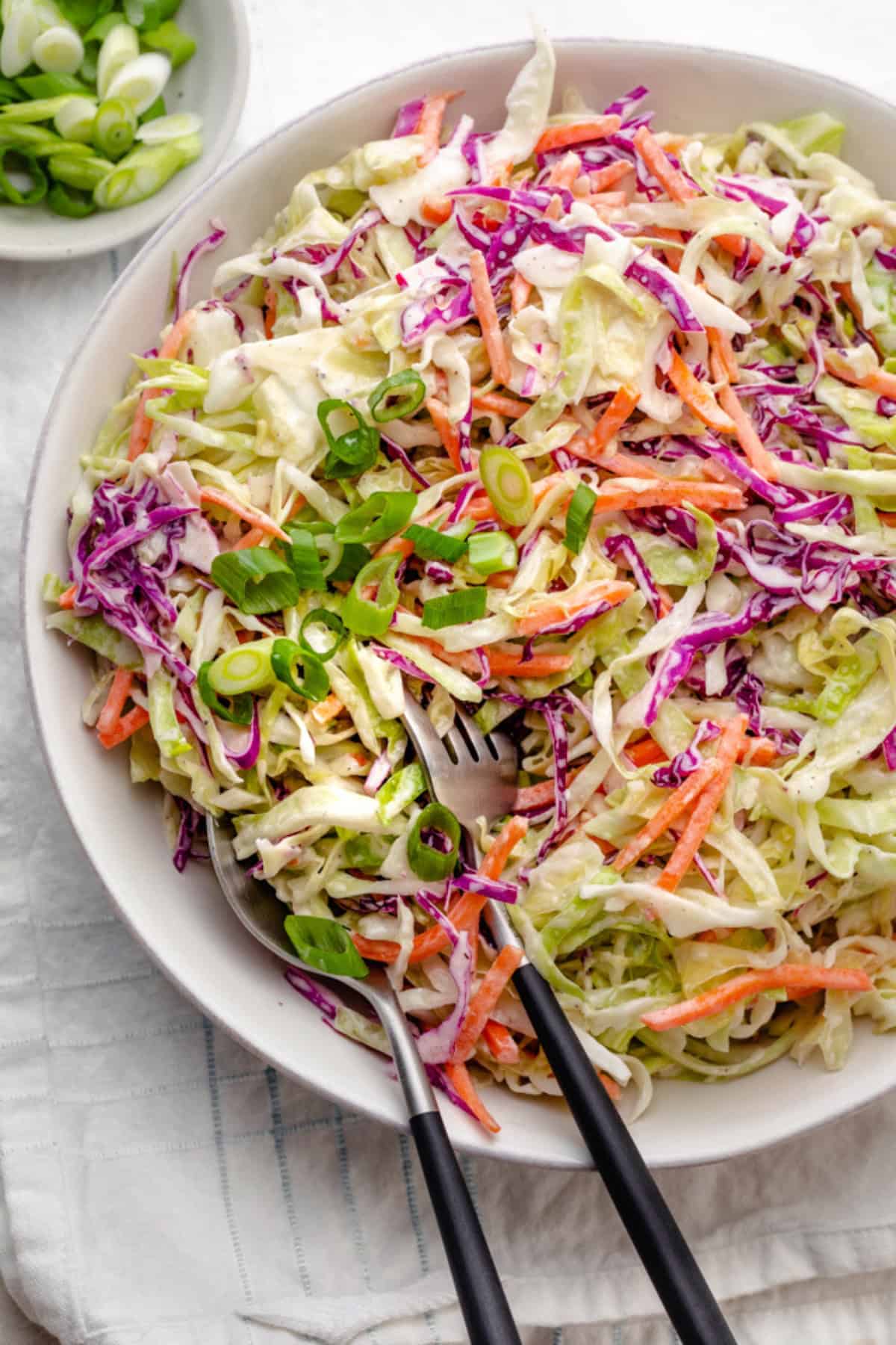 Healthy coleslaw in a bowl with fork and spoon set dipped inside.