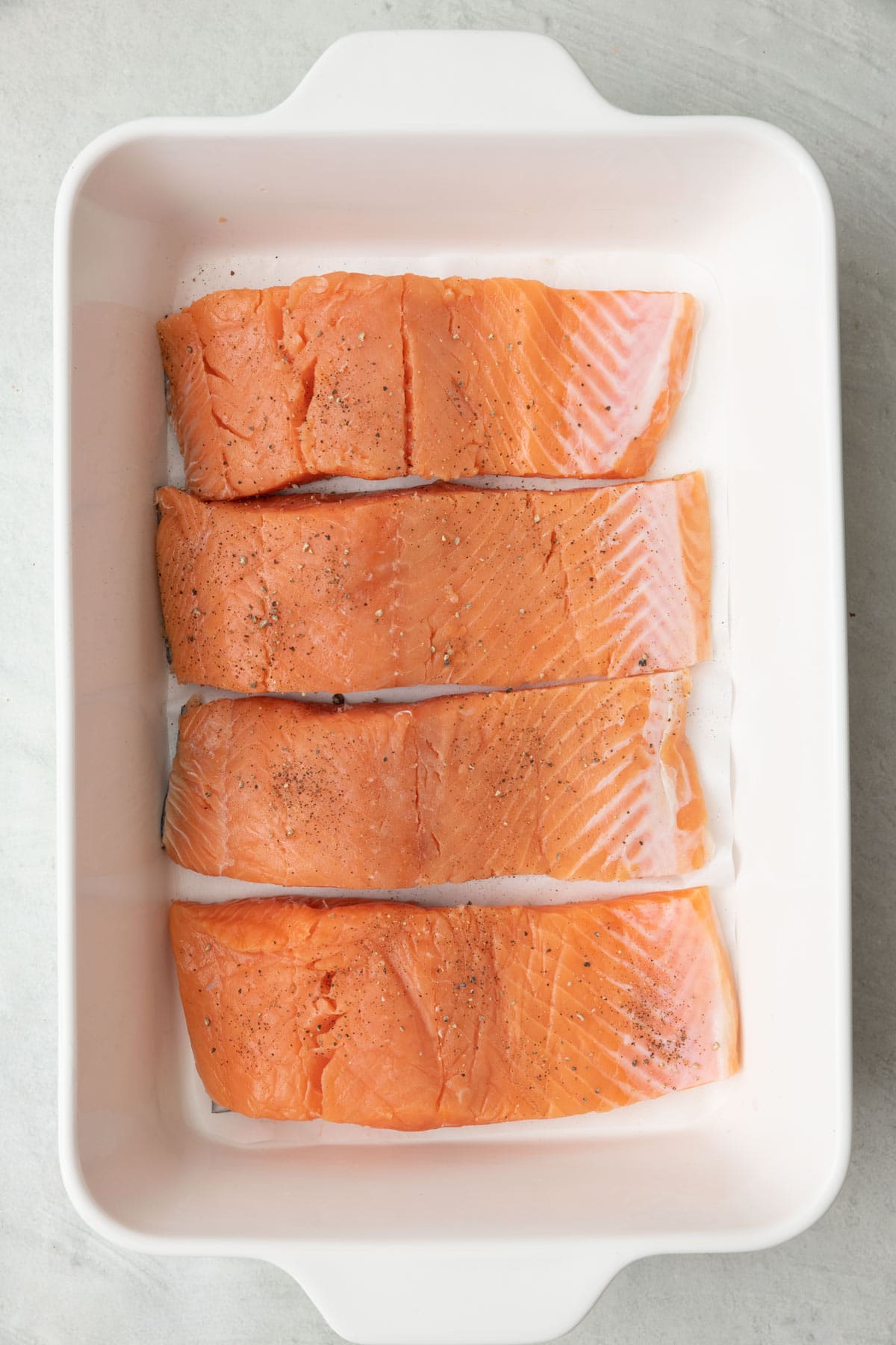 Salmon in a baking dish line with flat parchment paper.