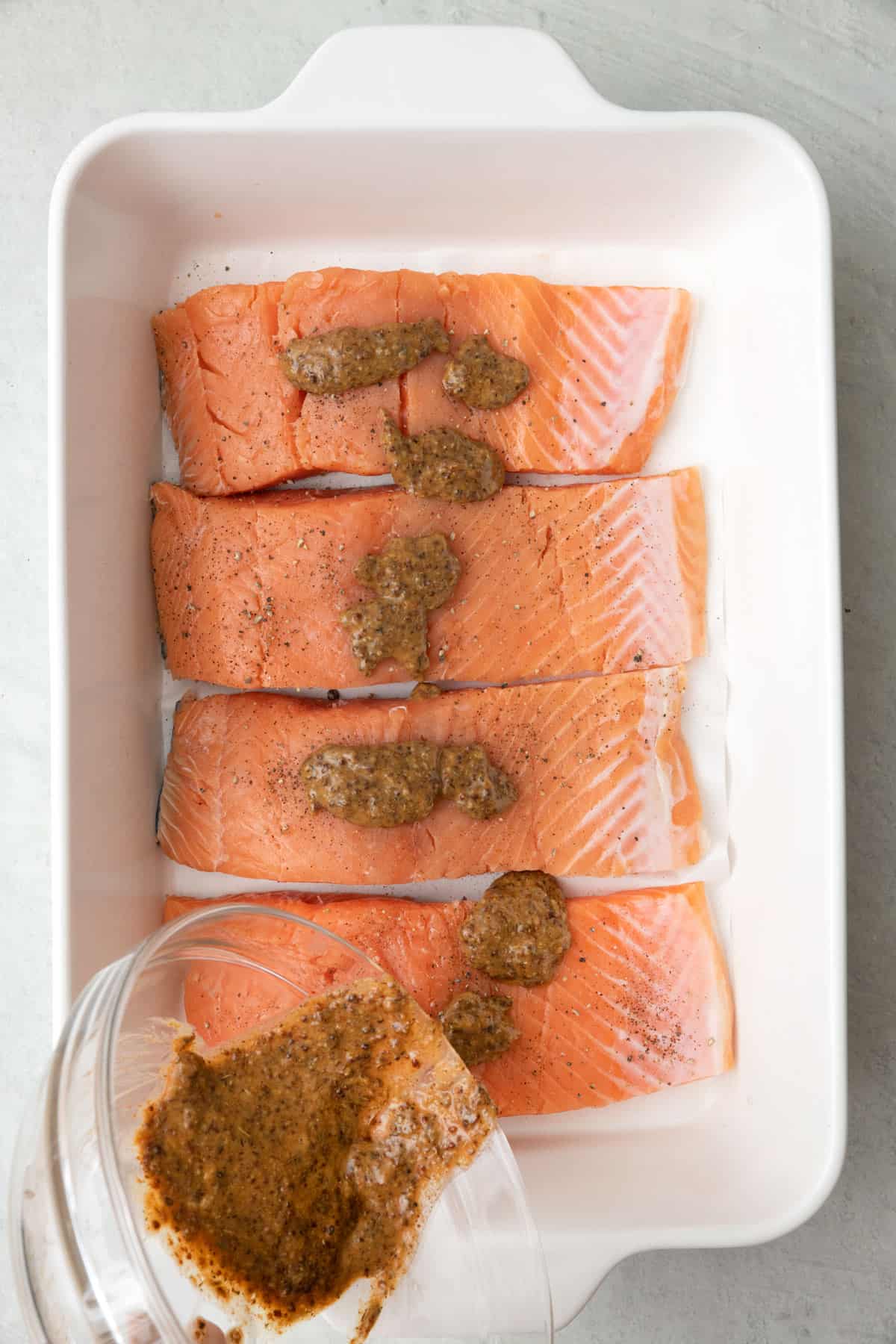 Pouring mustard mixture on top of salmon.