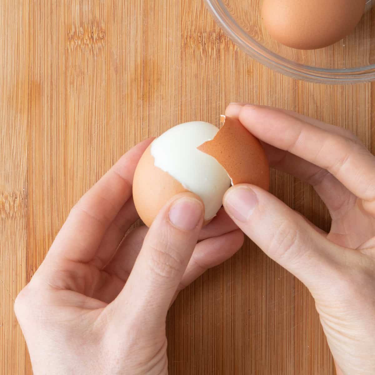 Holding the cracked egg in your hand using the other hand to peel off a large piece of the shell.