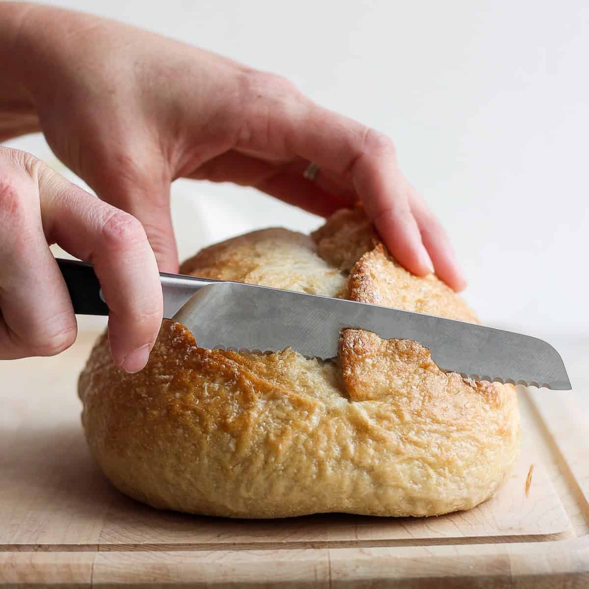 Loaf of bread on cutting board being cut with a serrated knife.